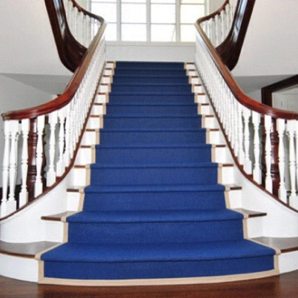 Blue custom stair runner installed on a grand curved staircase in a luxury home with hardwood stairs and white balusters.