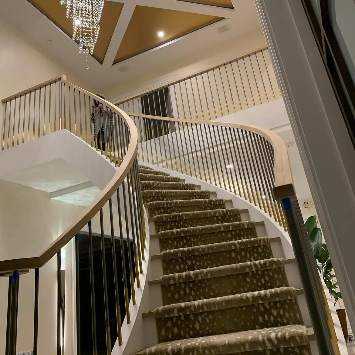 Custom patterned stair carpet runner installed on a curved staircase with modern metal railings in a luxury home.