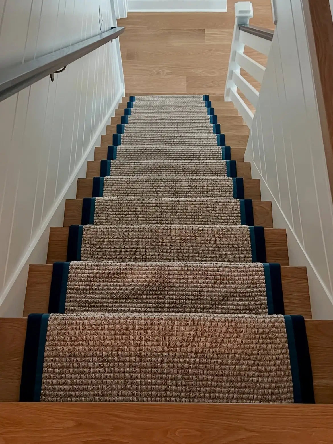Woven custom stair runner with navy border professionally installed on hardwood stairs in NYC.